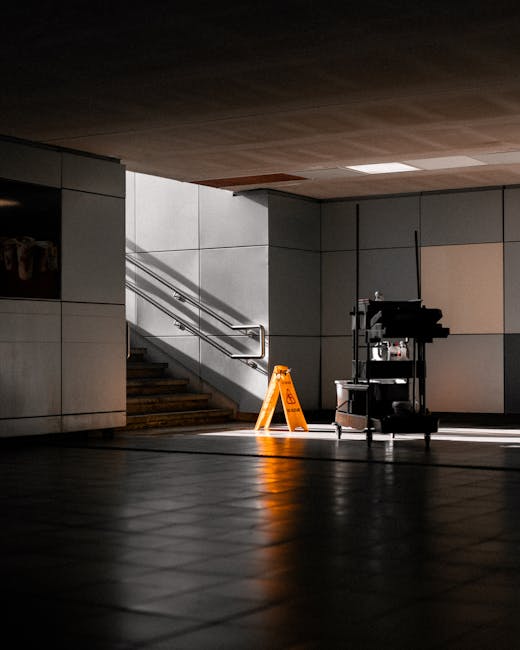 A person wearing yellow rubber boots and dark clothing is using a floor scrubber to clean the wet exterior entrance of a retail shop on Blackstock Road, Finsbury Park. The cleaning process involves a 